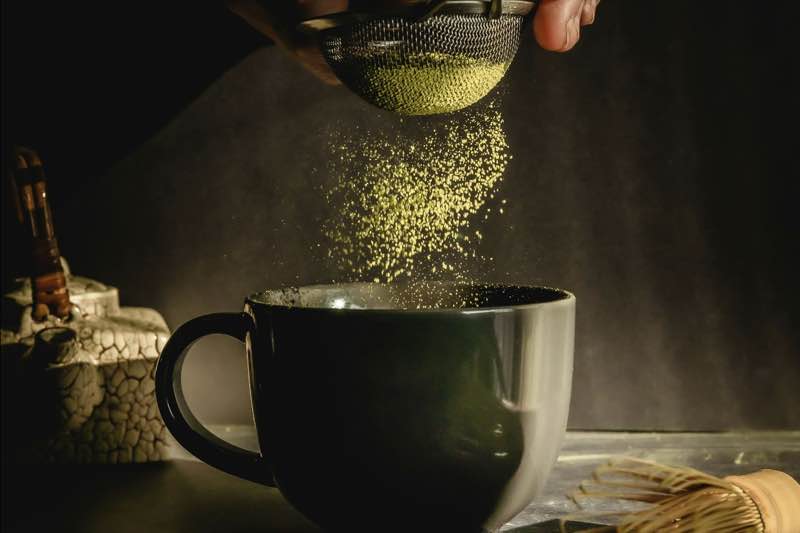 Matcha powder being sifted into a dark mug