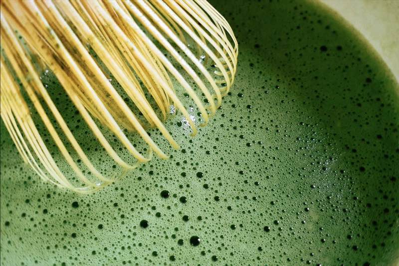 A bamboo whisk in a bowl of frothy matcha